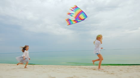 two little girls playing on the beach flying a kite