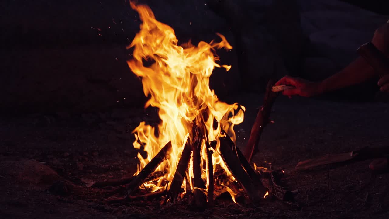 A man near the fire in the evening. Bonfire. Burning logs in orange flames. Slow motion