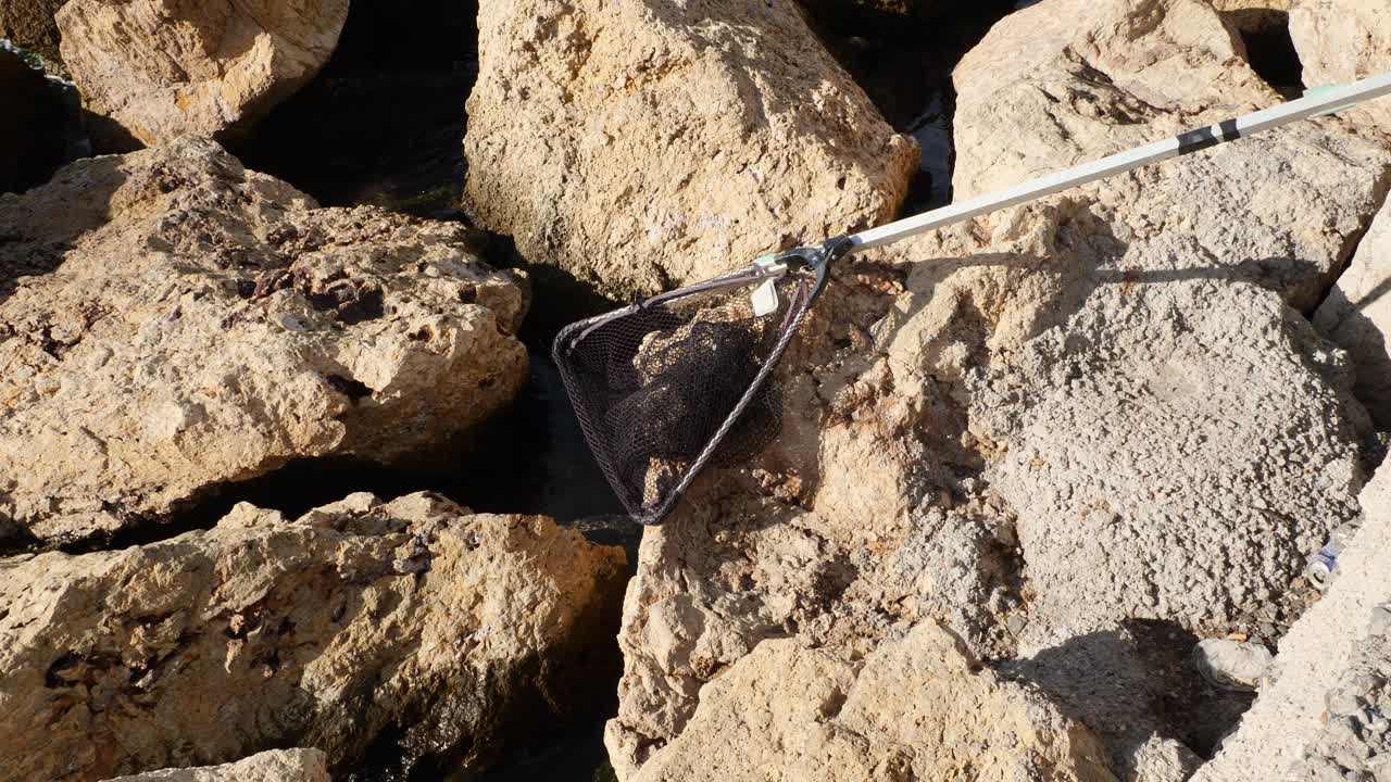 Zoom su una rete da pesca abbandonata sulle rocce, al rallentatore. Originariamente a 59,94 fps