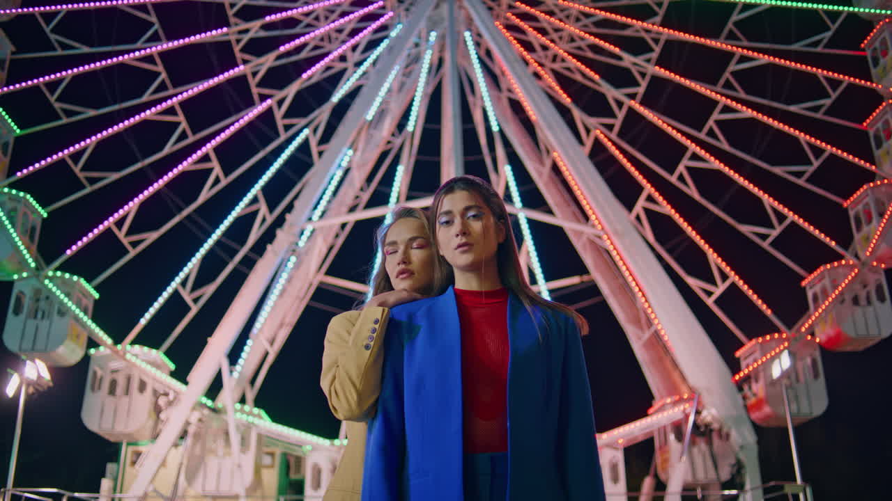Girlfriends posing ferris wheel at night. Two models resting illuminated funfair
