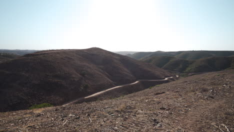 Small-barren-hills-and-dirt-trails-in-harsh-landscape-in-Algarve,-Portugal---Pan-shot