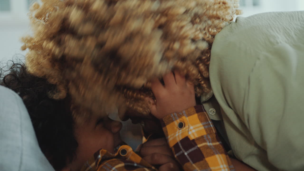 African American Mother Rubbing Noses with Joyous Little Son Lying on Sofa