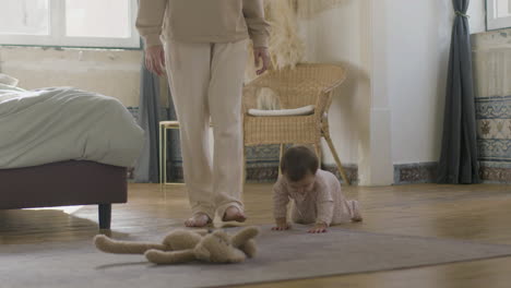 adorable bebé en pijama arrastrándose por el suelo del dormitorio mientras los padres la cuidan