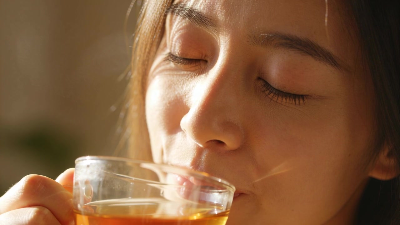 Percebendo vapor, mulher asiática adulta trazendo xícara de vidro, sorvendo e depois abaixando para relaxar em casa.