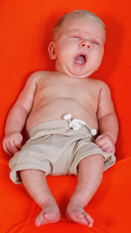 relaxed yawning baby boy lying in the orange chair. sand and swimming circle around the kid. vertical video