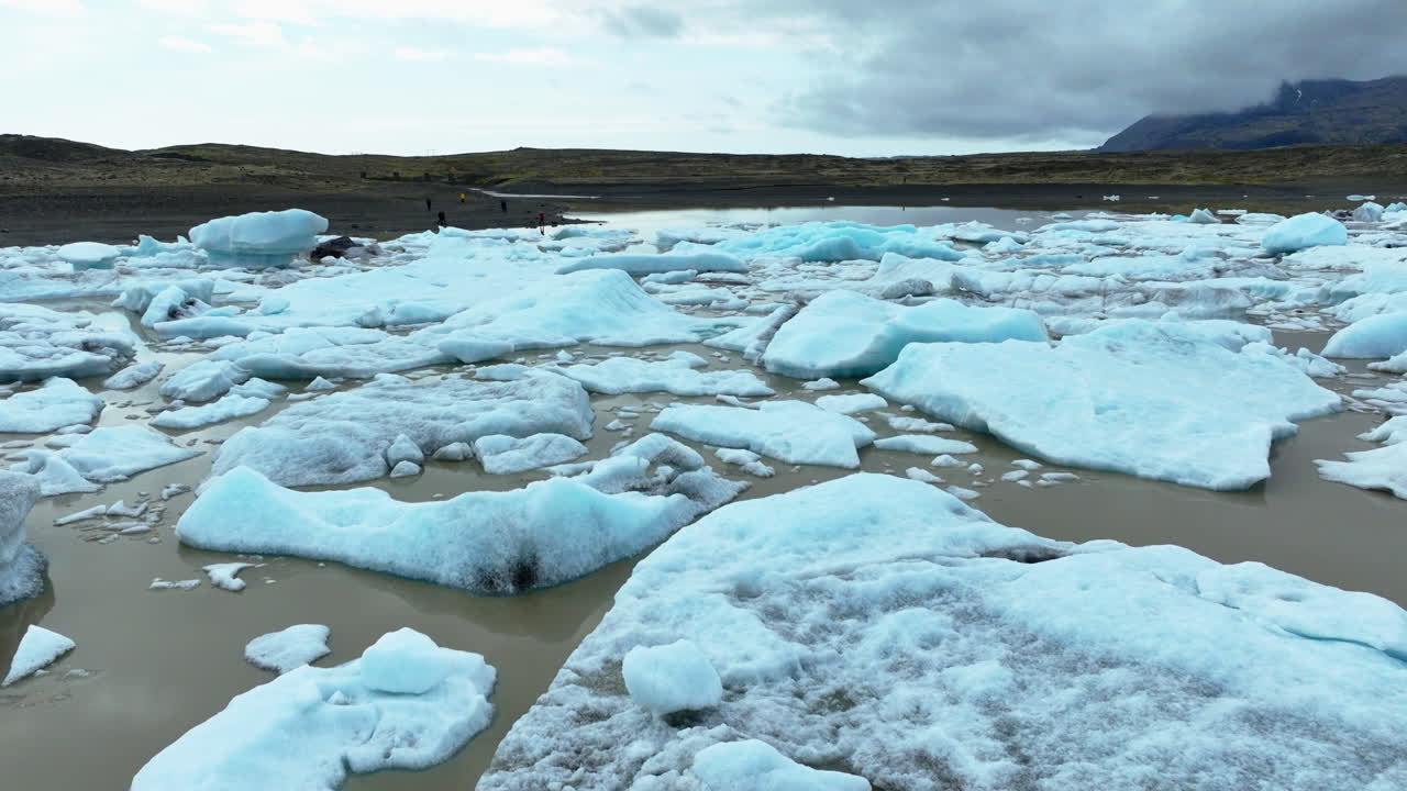 Drone shot flying over beautiful blue icebergs floating in a lake in front of a glacier in Iceland