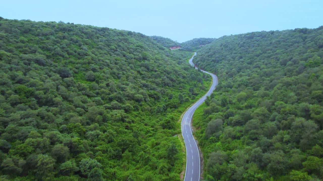 vista aérea de un avión no tripulado de una carretera a través de un bosque de selva verde exuberante con un telón de fondo montañoso durante el monzón en gwalior madhya pradesh india