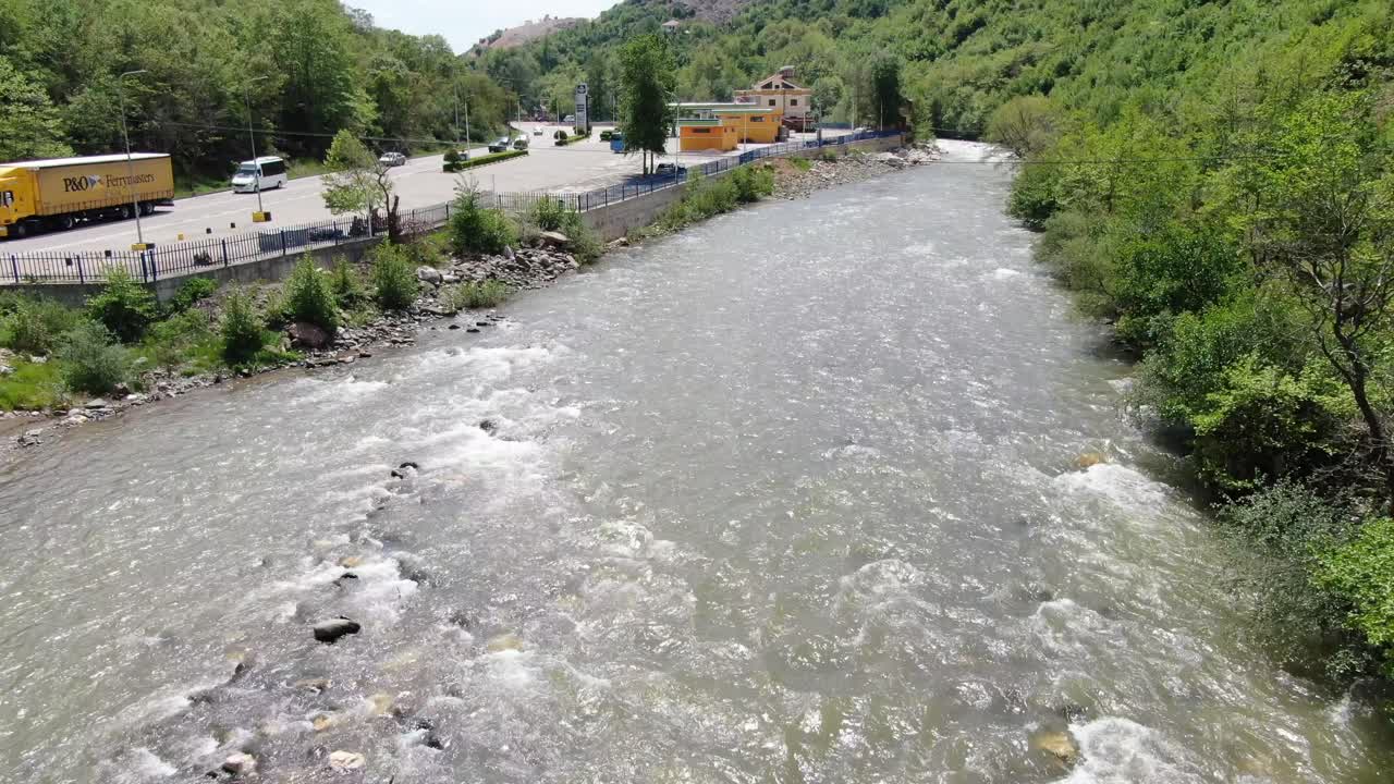 알바니아의 드론 뷰는 빠른 강과 그 에 있는 도로와 함께 지나가는 자동차와 함께 푸른 풍경 위를 날고 있습니다.