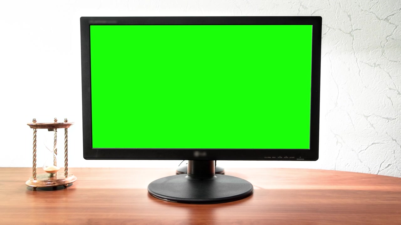 En dataskjerm med grønn skjerm står på et skrivebord på et kontor i en timelapse hyperlapse med fremoverbevegelse. Arbeidsplassdesign med et timeglass på venstre side.