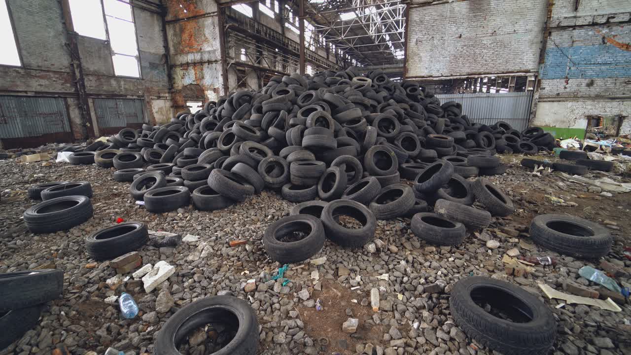 A bunch of car tires are in an abandoned high hangar with holes in the windows of building. View of old factory inside. Close-up.