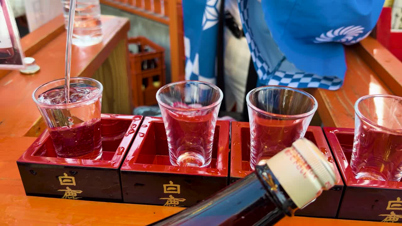 Primo piano di sake versato in bicchieri posti all'interno di tradizionali scatole di masu in legno rosso.