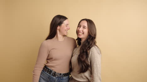 cheerful young women cuddling against beige backdrop