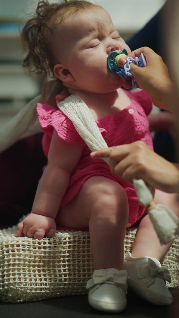 Close up of an infant resting in a supported position while the mother places a pacifier in the baby's mouth during a pediatric mobility and developmental therapy session
