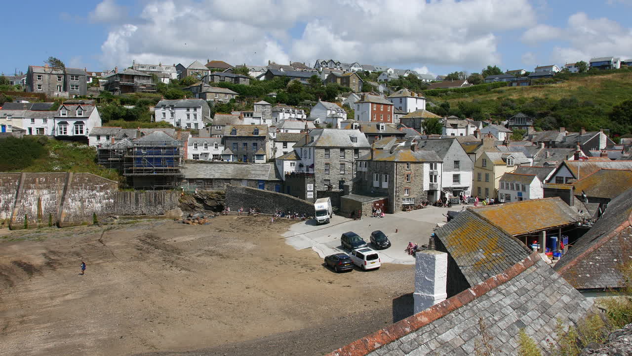 Una piazza del paese a Port Isaac, in Cornovaglia, con case in pietra raggruppate, veicoli parcheggiati e turisti che passeggiano nella zona del porto di marea nel cuore di Portwenn