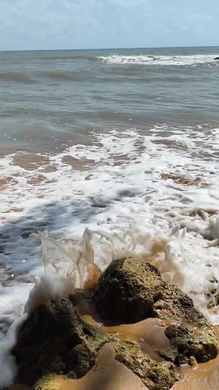 Onde oceaniche che si infrangono su una spiaggia rocciosa e sabbiosa.