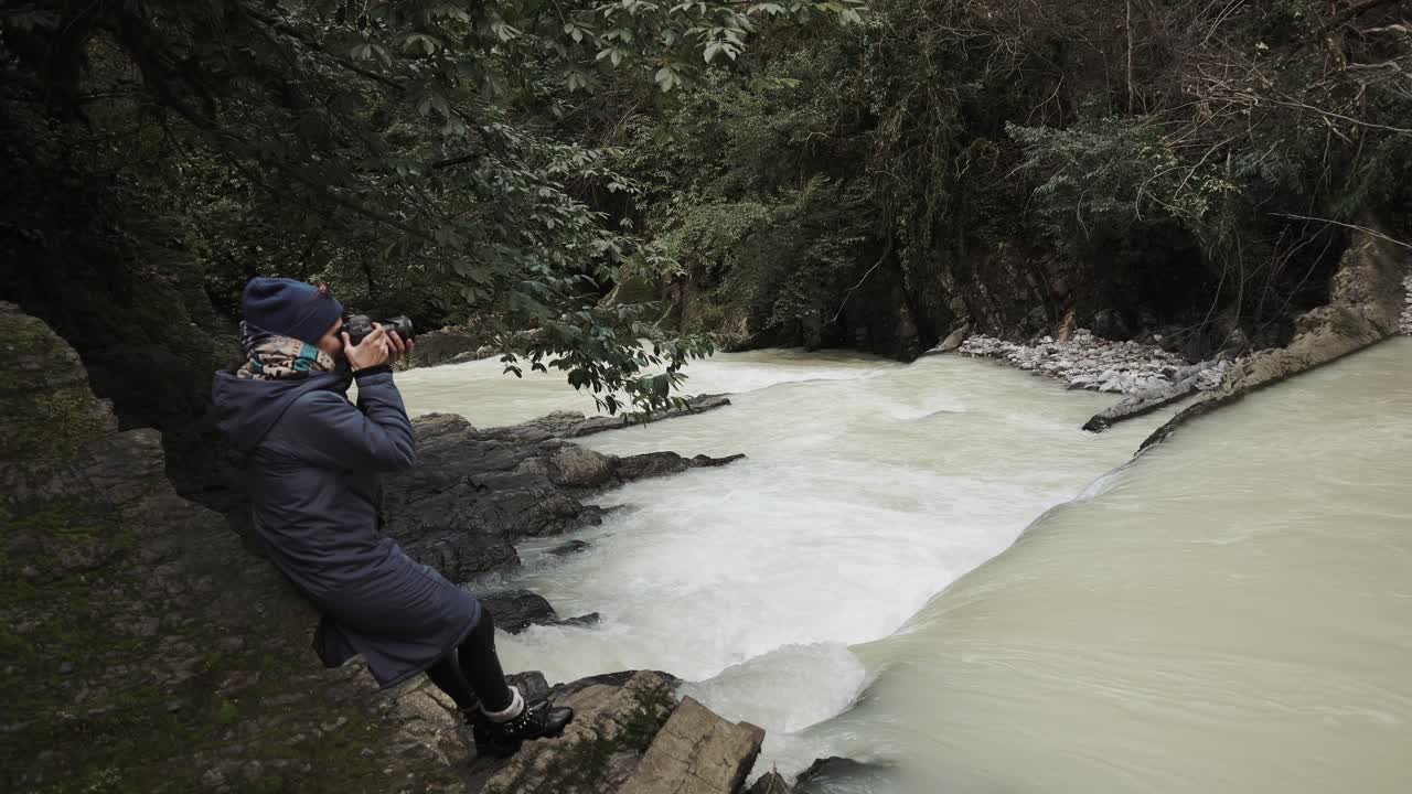 mujer tomando fotos de una cascada en un bosque