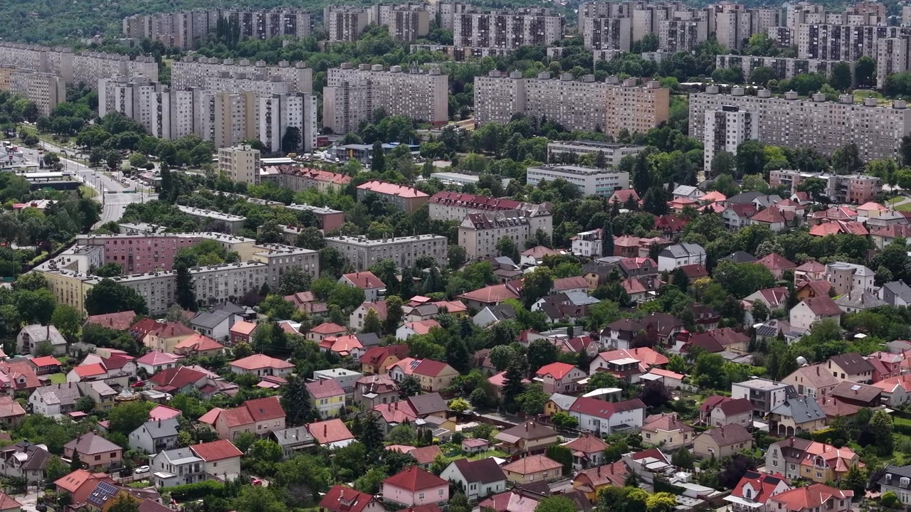 Uma vista aérea ampla mostra o contraste entre edifícios de apartamentos densos e um bairro residencial extenso com árvores abundantes.