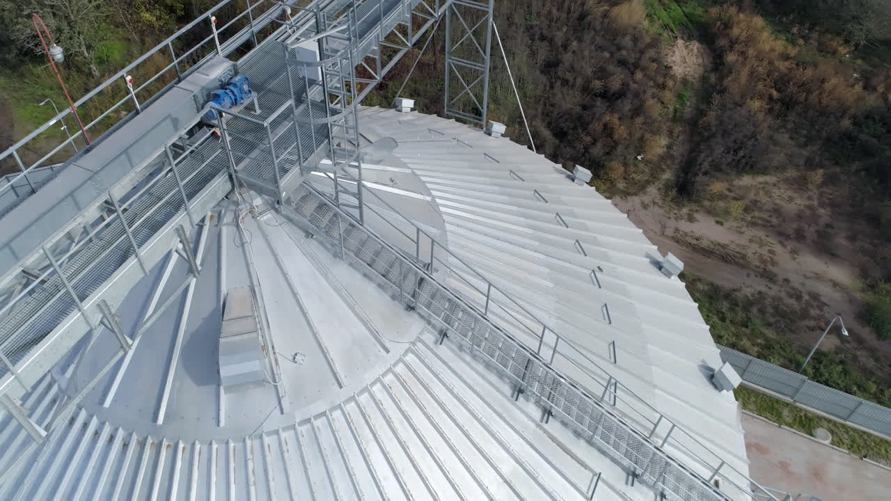 Large grain elevator. Silver granary from above. Aluminum container. Agricultural equipment for storing crop. Top aerial view.