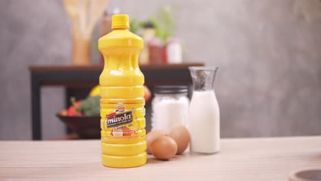woman took the bottle of minola cooking oil with eggs and milk on a table  - close up shot