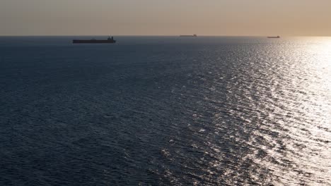 container ships wait on horizon as drone descends to blue ocean water