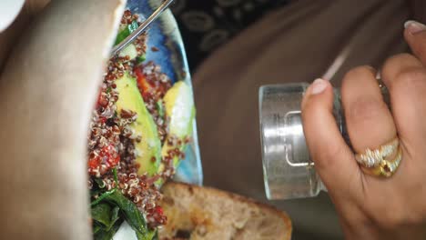a close-up of a hand seasoning a healthy meal with quinoa, avocado, and toast