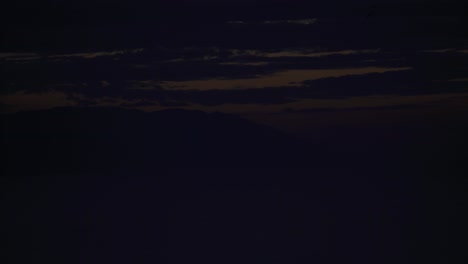 timelapse of the sun setting into the ocean behind a mountain with a golden sky and moving clouds as the scene fades to black