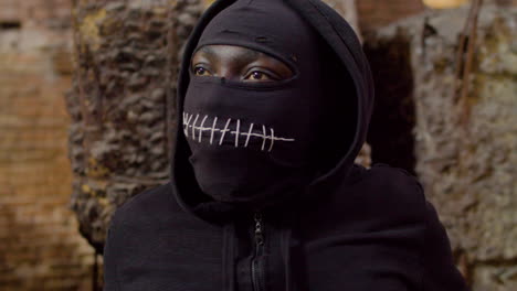 close up view of man wearing black balaclava and holding an ax in a ruined building 1