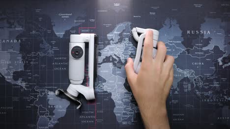 La-Mano-Toma-El-Moderno-Cardán-Compacto-Insta360-Flow-Y-Osmo-Mobile-Plegado-Sobre-El-Mapa-Mundial-Como-Fondo