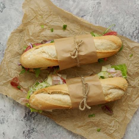 sándwiches con jamón, verduras frescas y hierbas servidas en papel marrón para hornear sobre fondo de hormigón