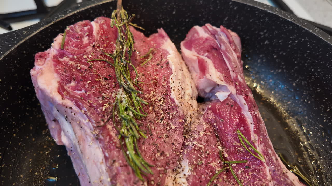 Big red beef stake on a black pan with rosemary ready for cooking, black pepper on top