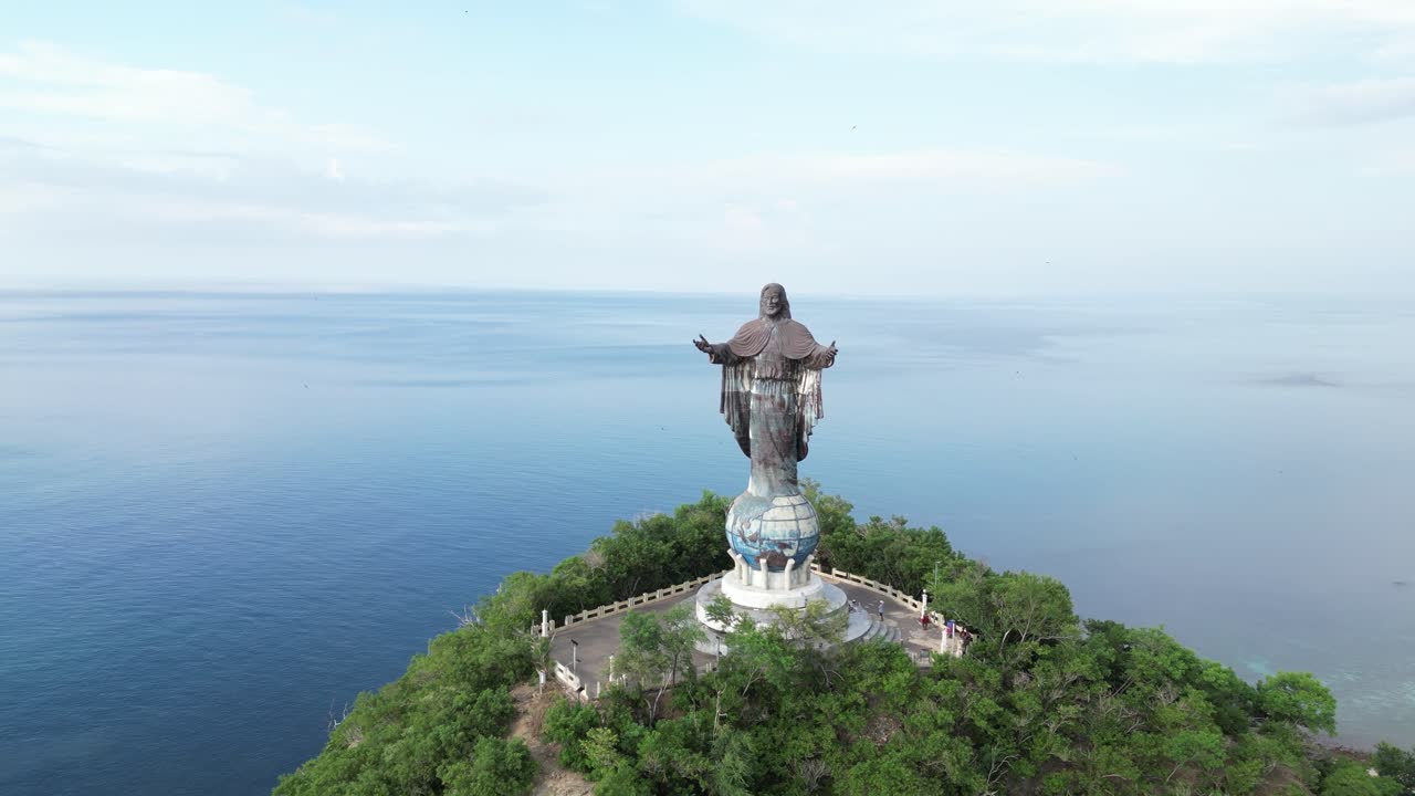 Aerial view of a large Jesus Christ statue on a hilltop overlooking the ocean and greenery.