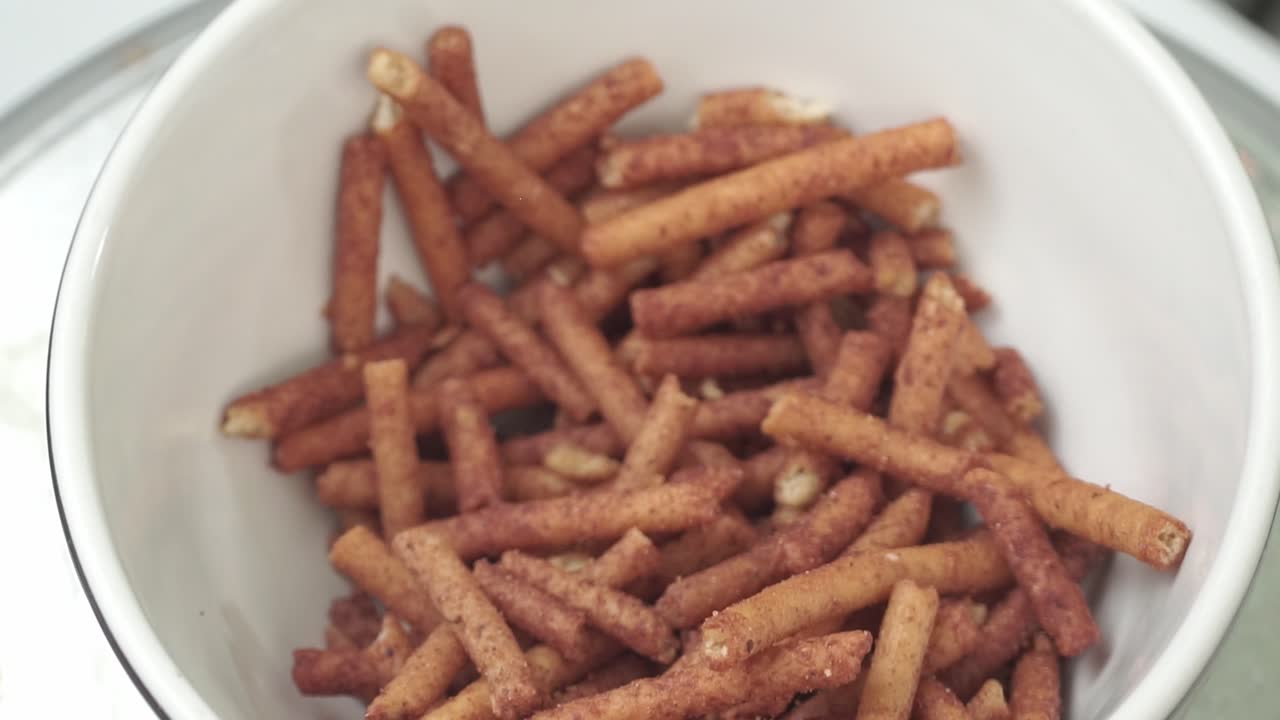 A white bowl full of seasoned pretzel sticks, a savory party snack