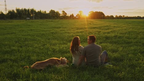 couple and dog enjoying sunset in a field