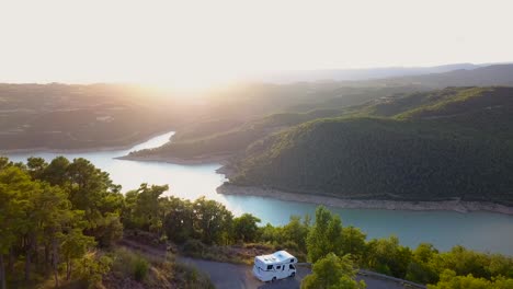 drone flying forwards revealing a caravan parked with incredible views of a blue and turquoise lake surrounded by dense green forest