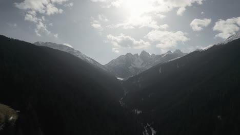 Aerial-drone-flying-over-alpine-mountains-covered-in-forests-with-rocky-mountain-formations-in-the-distance-on-a-warm-and-beautiful-sunny-blue-sky-winter-day