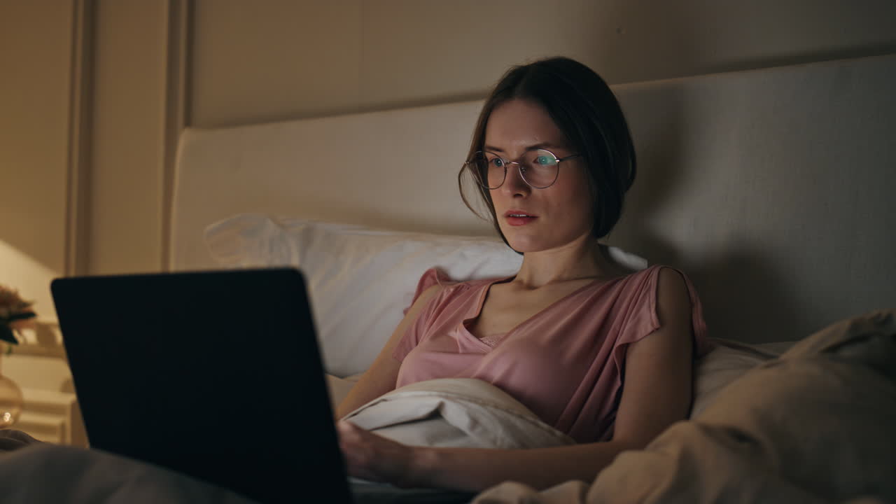 Glad kvinne surfer på laptop hjemme om natten, nærbilde. Smilende jente skriver melding.