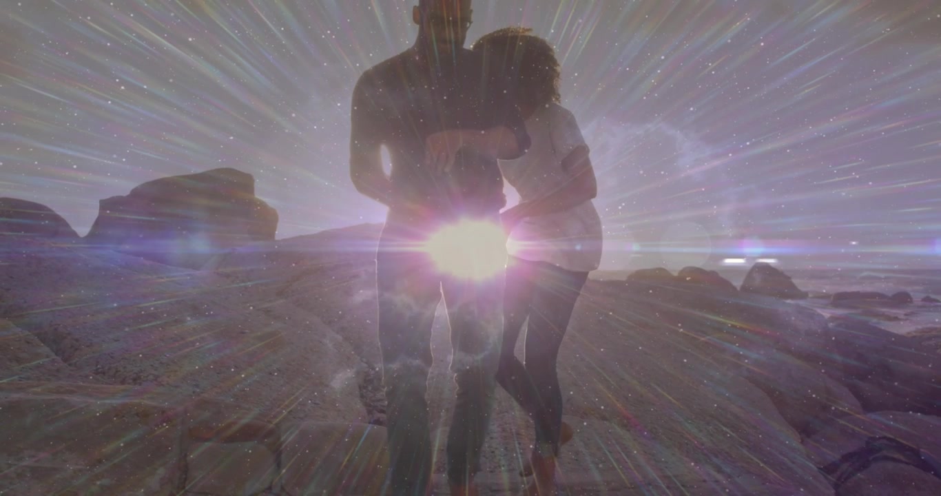 Coppia che cammina verso la telecamera su una costa rocciosa, il sole crea un bagliore e un effetto stella sovrapposto, vivendo un momento romantico.