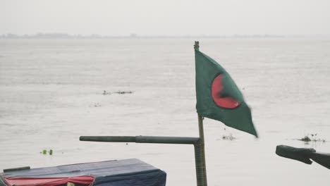 a bangladeshi flag is flying in a boat near river coast