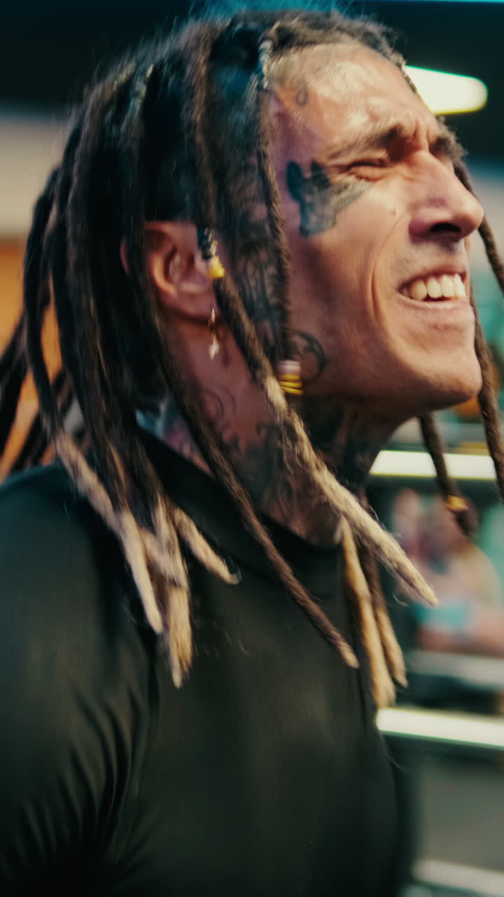 Uomo con dreadlock e tatuaggi che solleva pesi in palestra.
