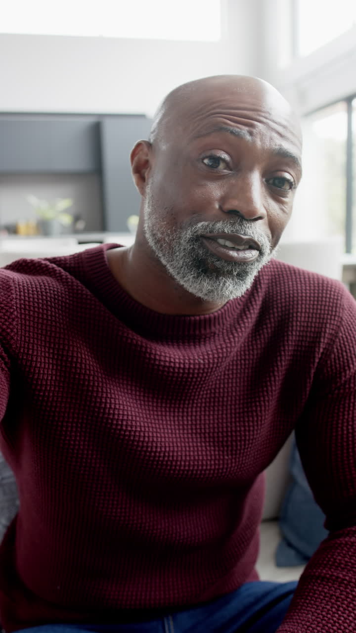 Vidéo verticale d'un homme afro-américain mature et heureux faisant un appel vidéo et saluant de la main, au ralenti