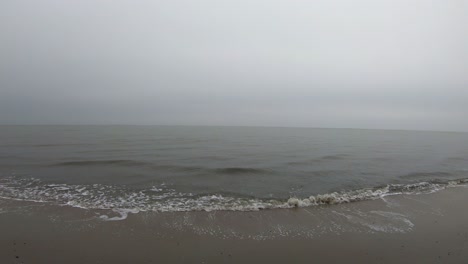 Small-ocean-waves-crashing-on-the-shore-on-a-rainy-day