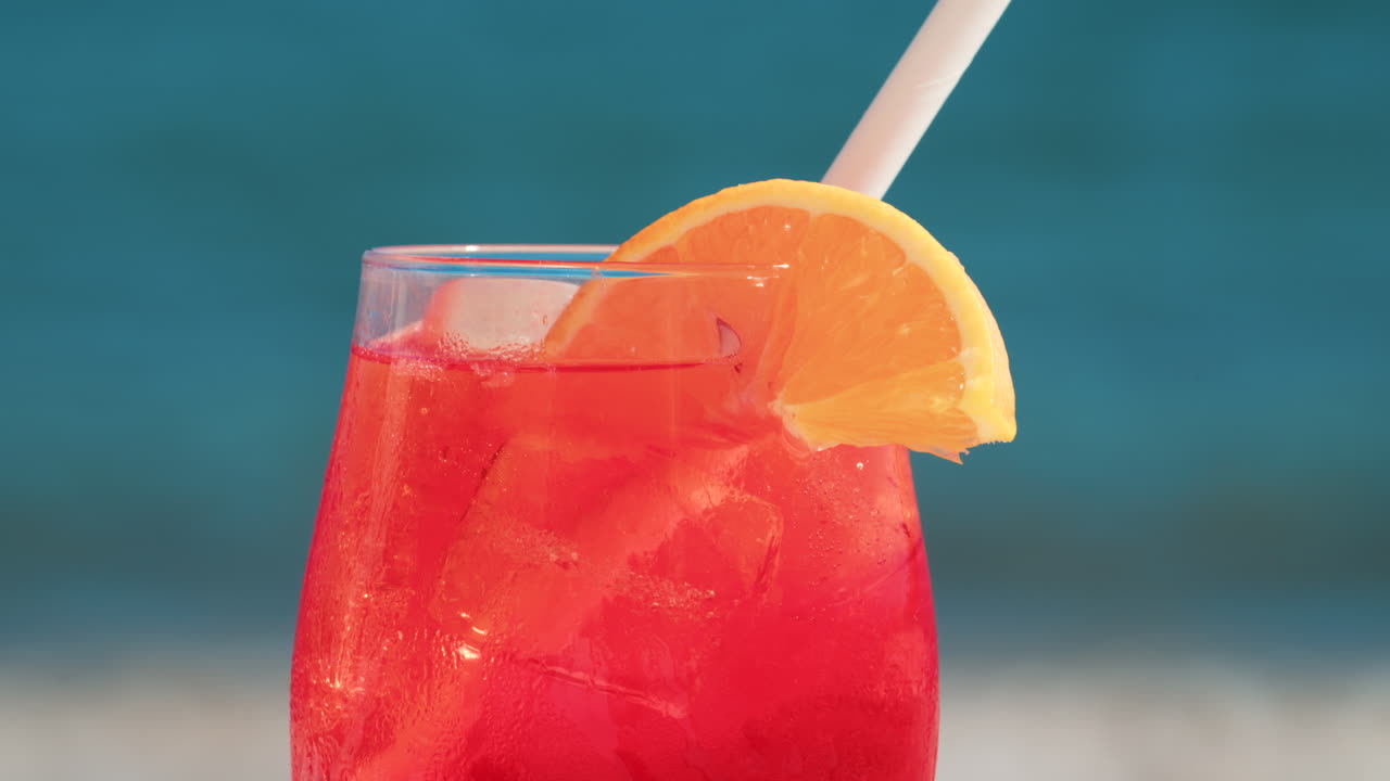 Close up of a refreshing red orange cocktail with orange slice and ice cubes, captured outdoors on a sunny day in Cannes