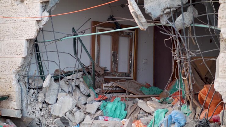 Large hole in a house wall in Gaza reveals debris, twisted metal, and remnants of a former living space.