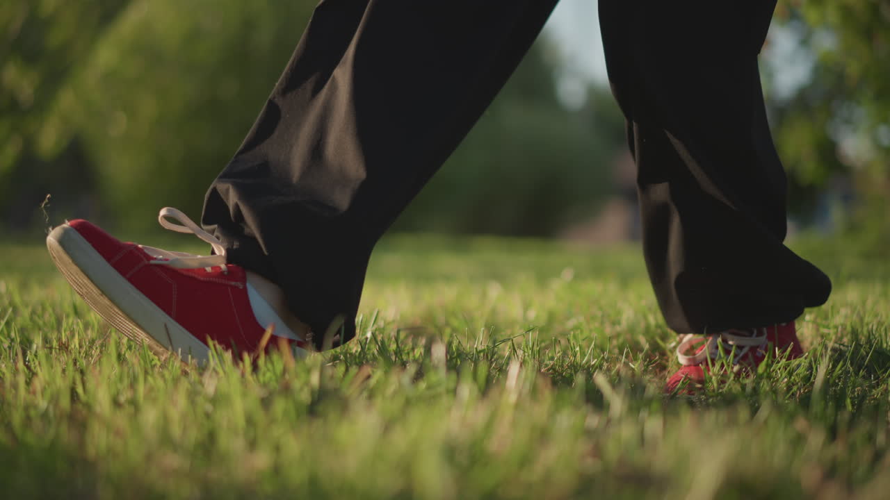 closeup red sneakers in park sunset showing steady rhythmic steps across meadow, slowpaced rehearsal focusing on stride, balance and timing, warm golden light, casual black pants, calm reflective