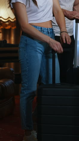 couple with travel bags. woman and man put their suitcases and sit on a sofa after the journey. young couple arrives into the hotel. view from the door. vertical video