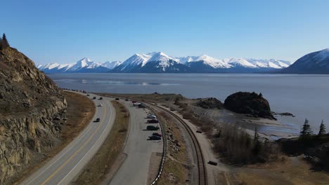 4k-drone-ascending-above-a-parking-lot-and-railroad-tracks-by-the-shoreline-showcasing-white-capped-mountains-on-a-sunny-day-with-a-view-of-the-bay-in-anchorage-Alaska