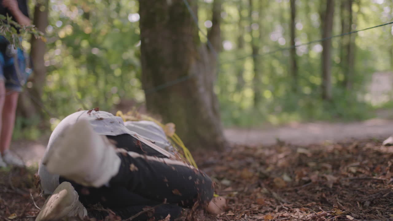 niños en un campamento de verano caminan por el suelo. entrenamiento para pasar obstáculos arrastrándose por el suelo. una niña cae en el bosque en una tarea de campamento