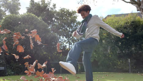 happy african american boy in scarf playing with fallen leaves in garden, slow motion