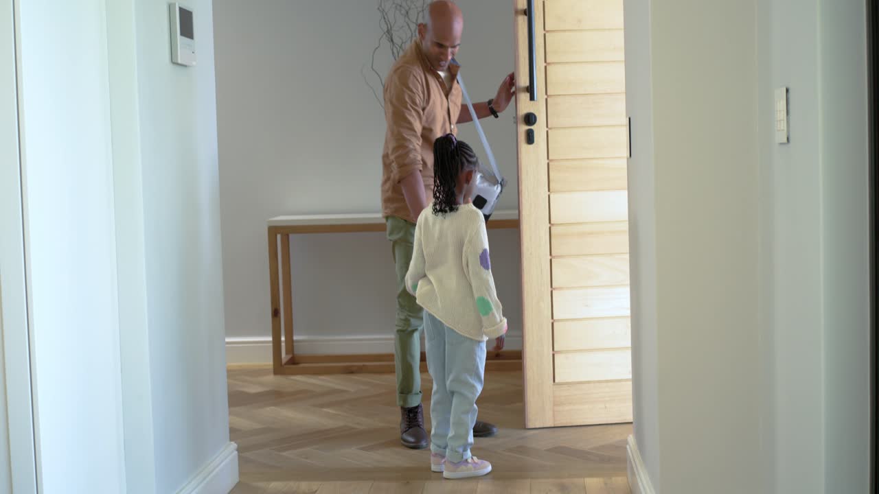 Dad and African American child hugging after door opening, entering with bag and papers in hallway
