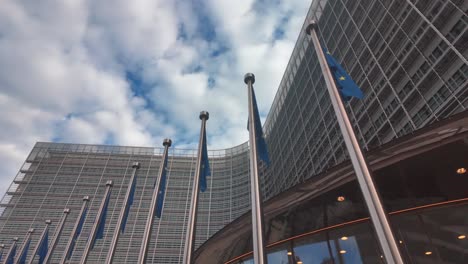 upward view of berlaymont building and eu flags under cloudy sky